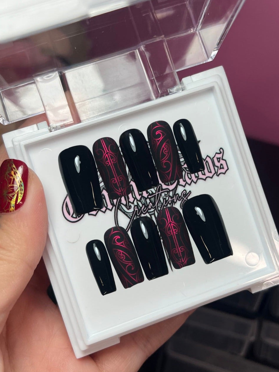 Set of black and sangria nail art designs in a clear case held by a hand.